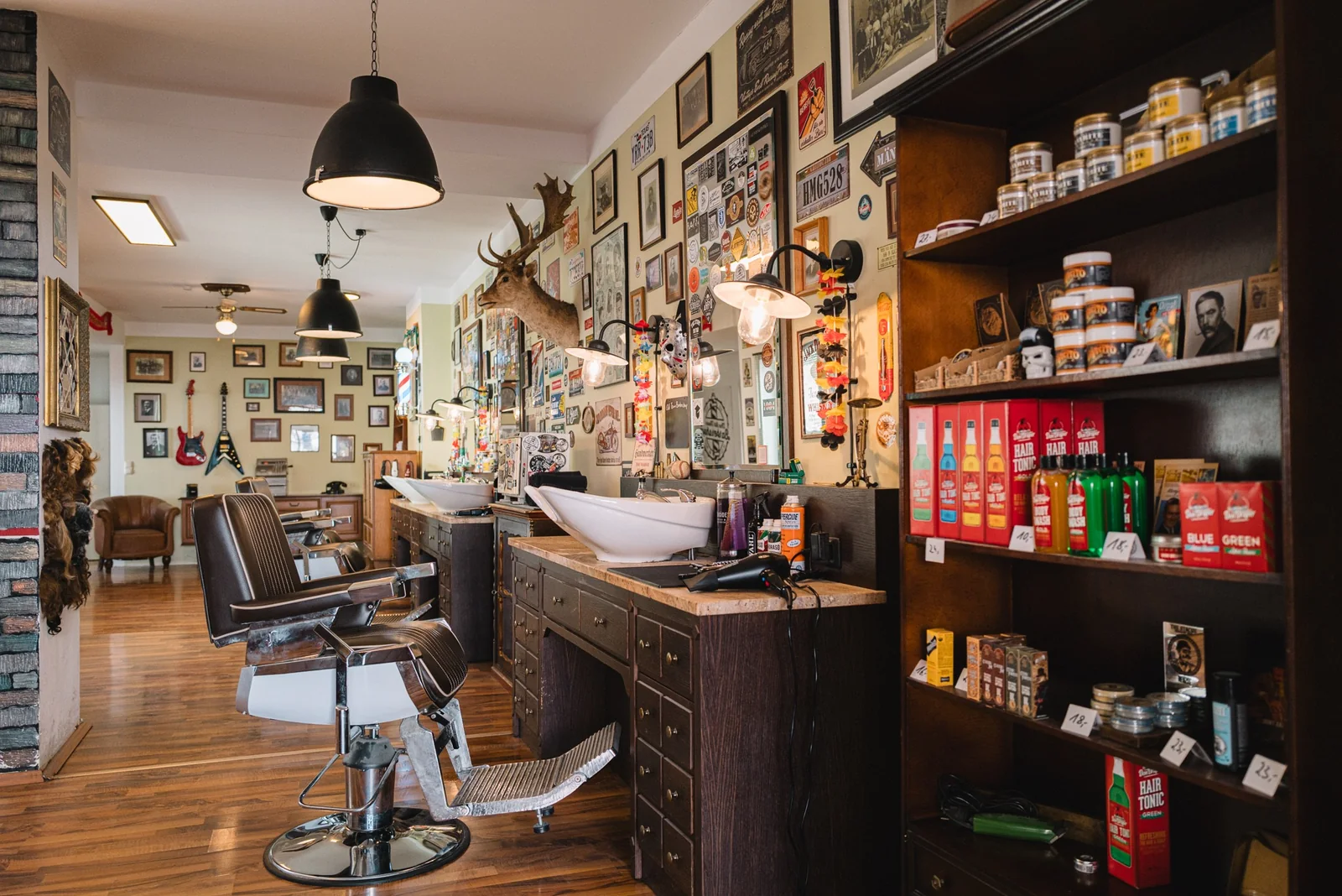 Der Laden: Barberstühle, Regale mit Pomaden, ein Hirschgeweih und Lampen über den Plätzen